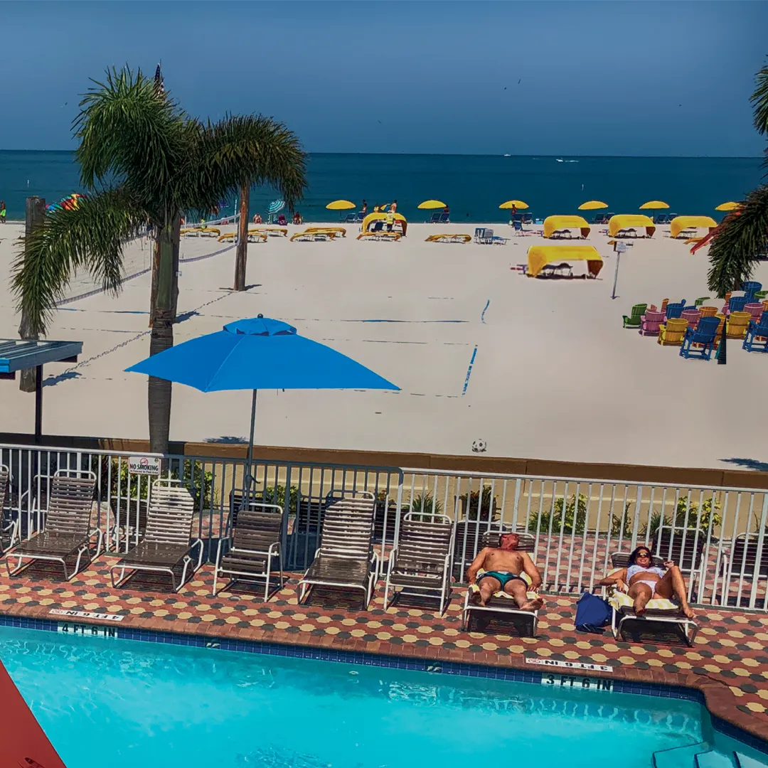 A balcony view showcasing a beach and pool at Plaza Beach Resorts, St. Pete Beach, Florida, under a clear blue sky.