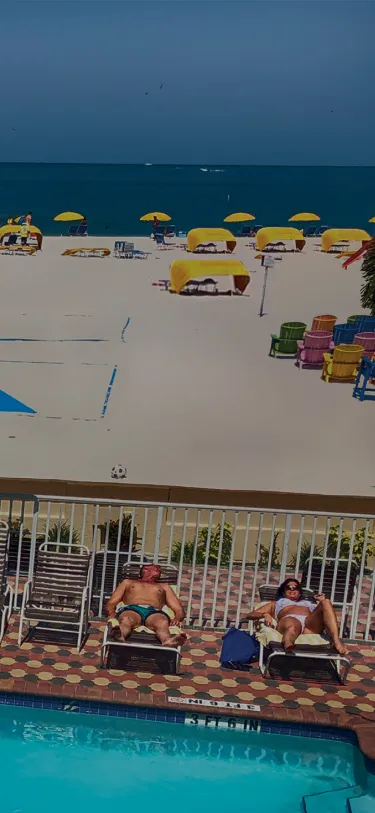A balcony view showcasing a beach and pool at Plaza Beach Resorts, St. Pete Beach, Florida, under a clear blue sky.